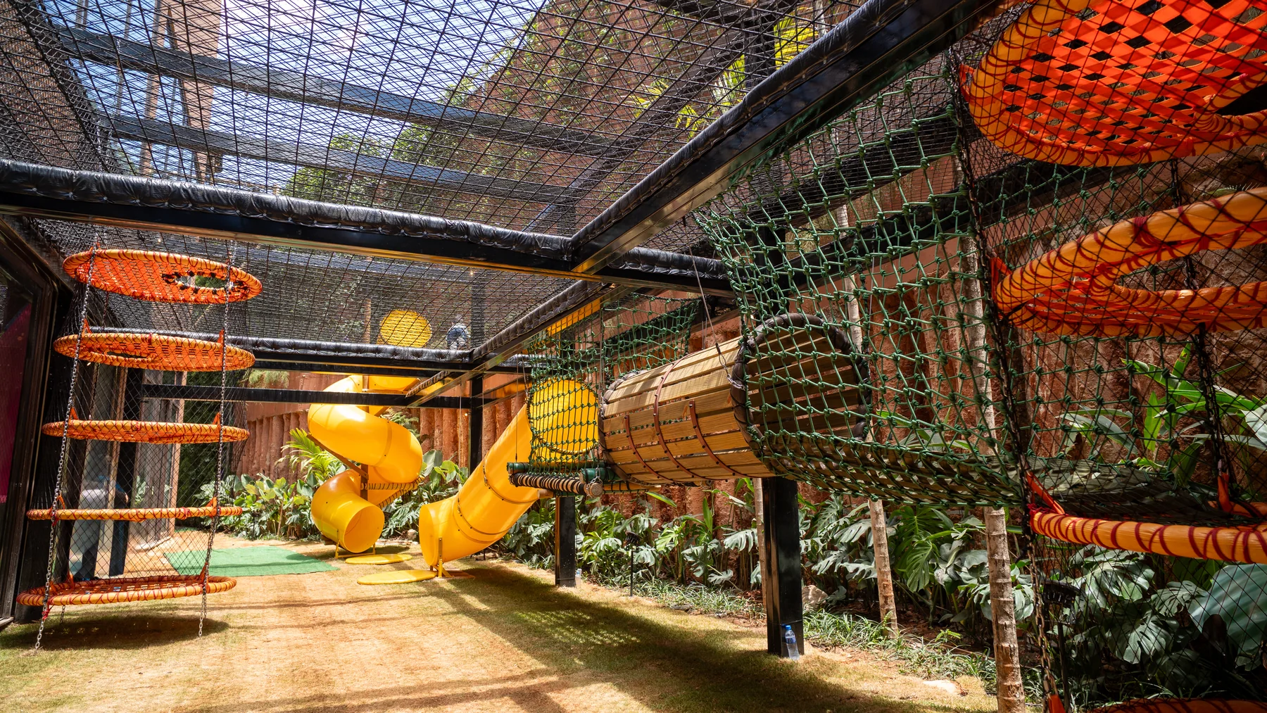 Parque externo com redes, escorregador amarelo e vegetação