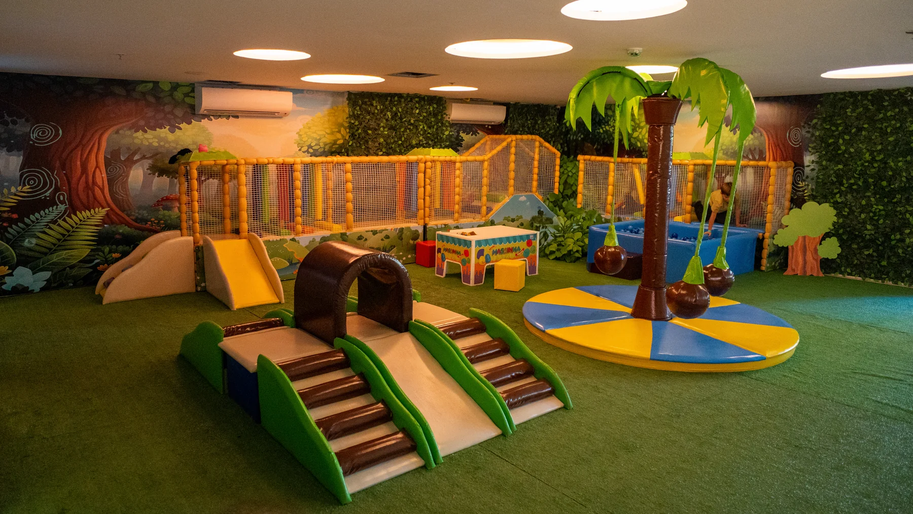 Espaço kids interno com brinquedos acolchoados e tema de floresta
